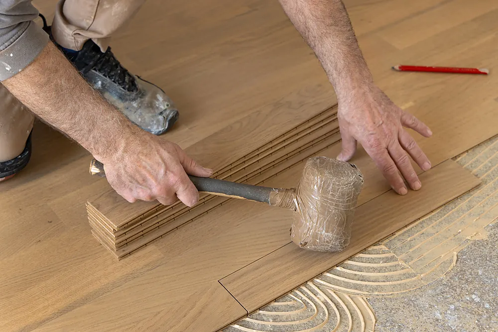 Installer tapping a hardwood board into troweled adhesive in Sioux Falls, SD